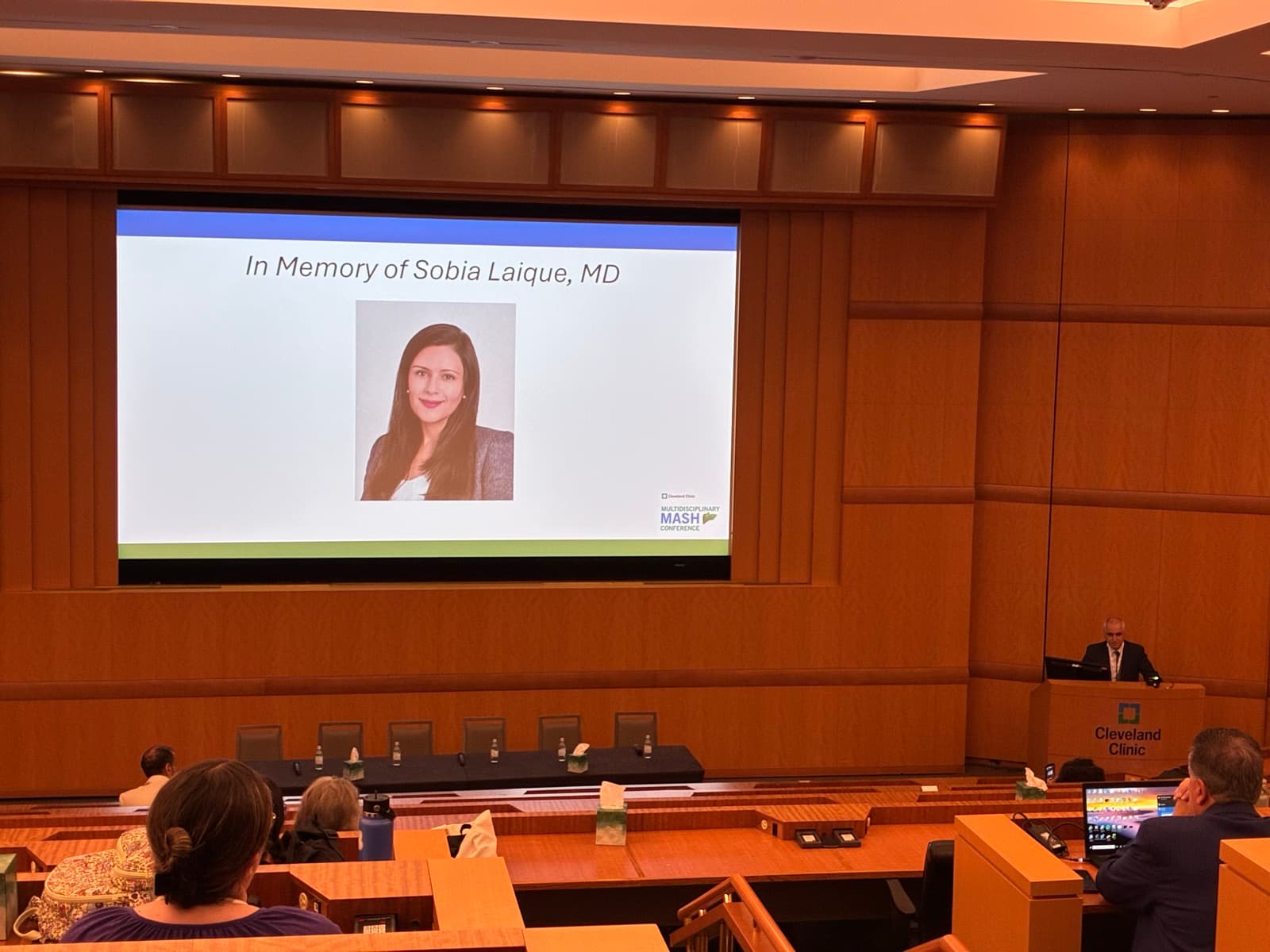 The auditorium during a moment of honor, with a slide reading In Memory of Sobia Laique, MD